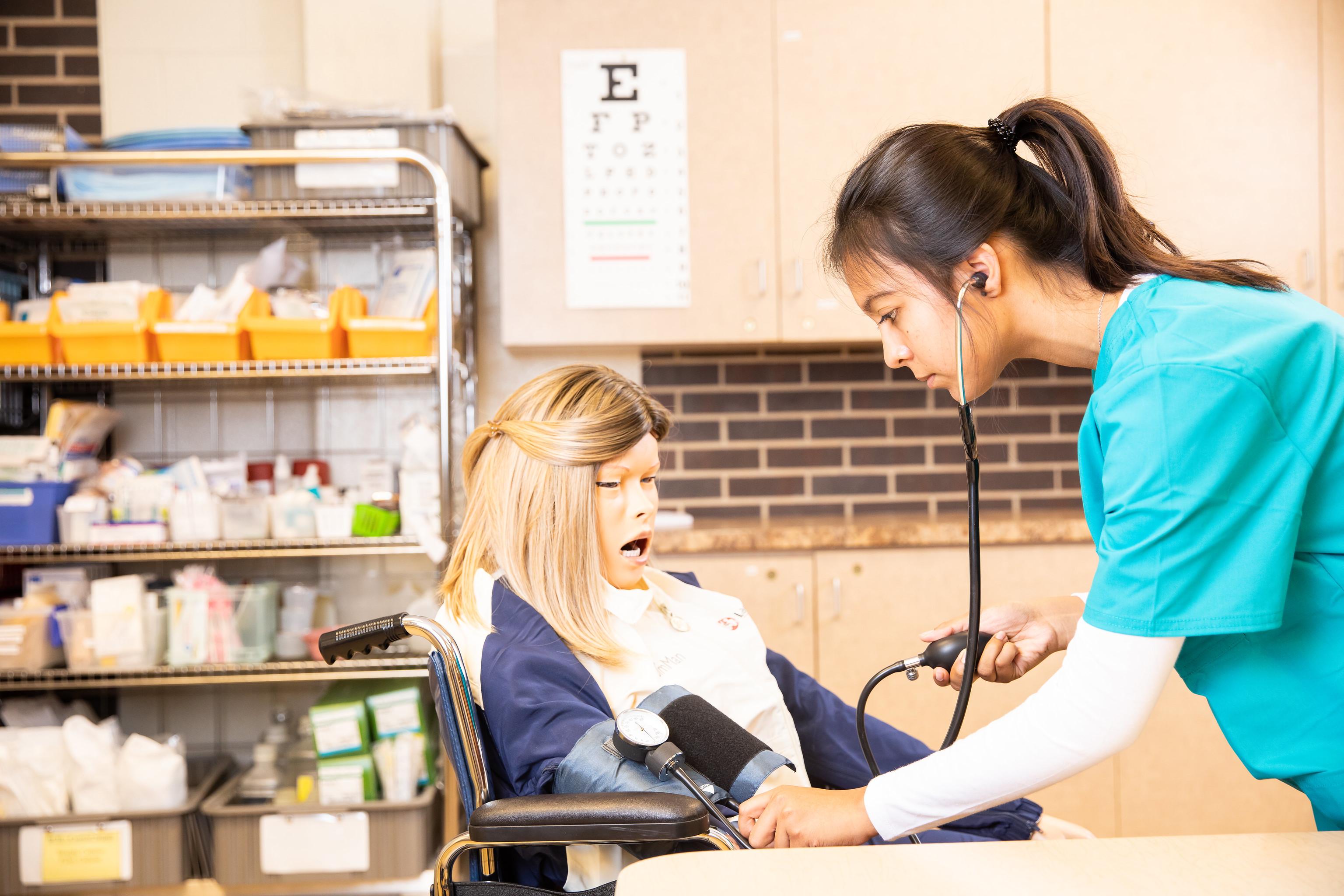 Nursing student practicing taking vitals on mannequin