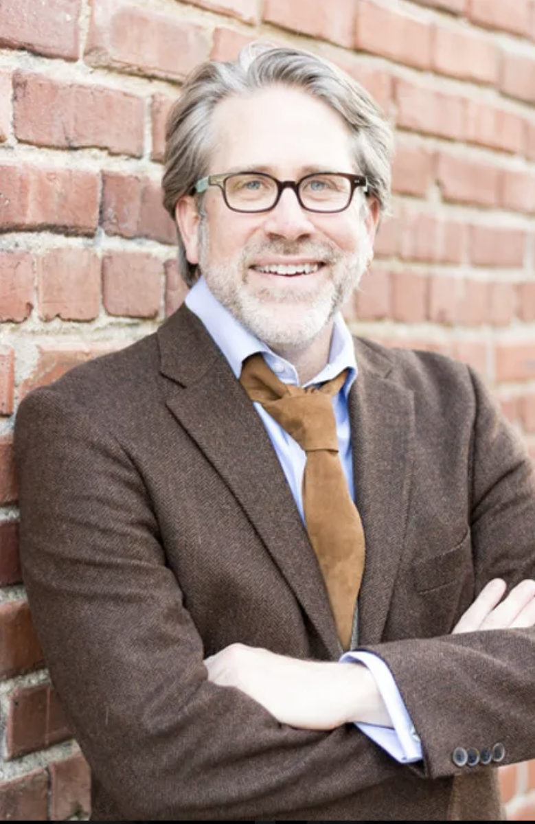 man posing for a photo against a brick wall with glasses on his face